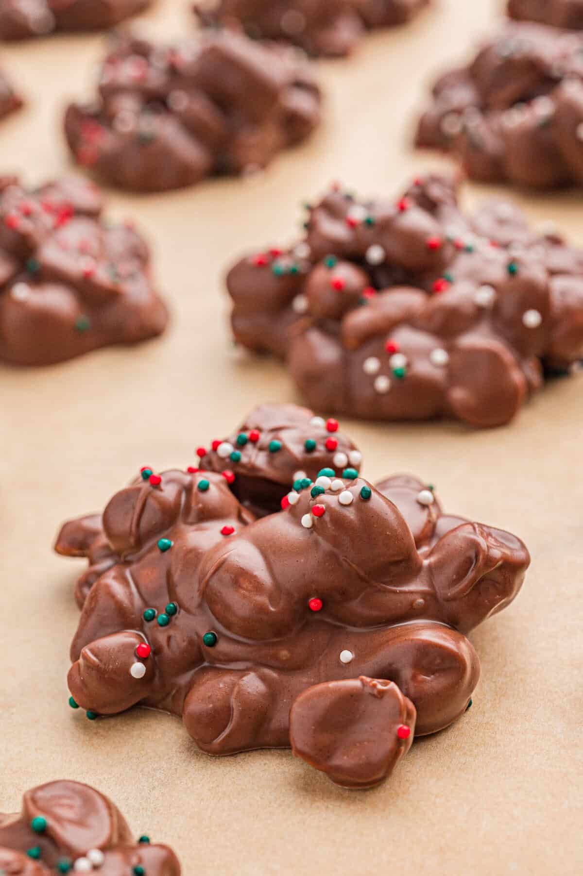 Rows of crockpot candy, chocolate peanut clusters, with Christmas sprinkles on parchment.