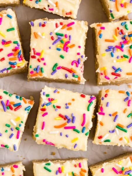 Top-down view of frosted sugar cookie bars with rainbow sprinkles, sliced into squares.