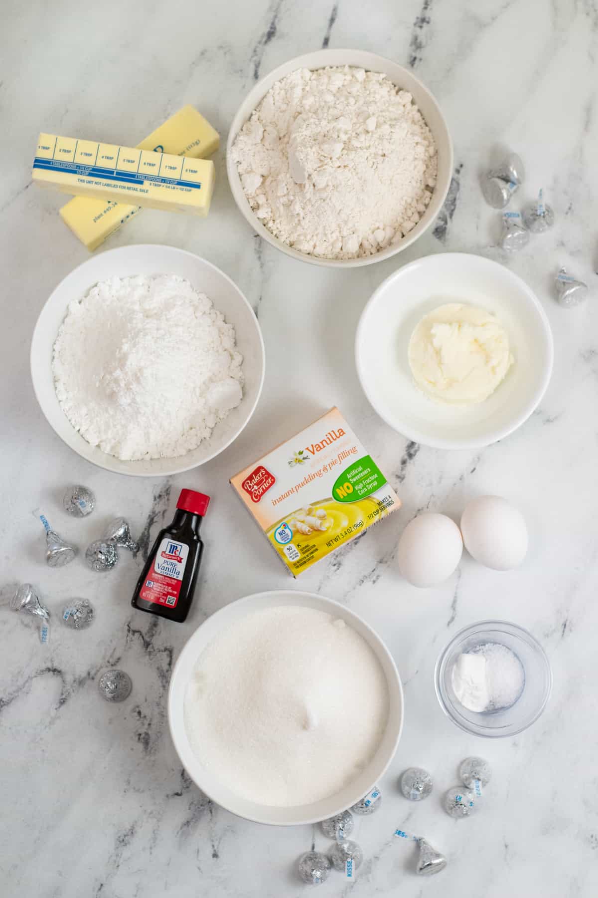 Ingredients on countertop: two sticks of butter, flour, granulated sugar, shortening, vanilla extract, box of vanilla instant pudding, 2 eggs, salt, baking powder, and milk.