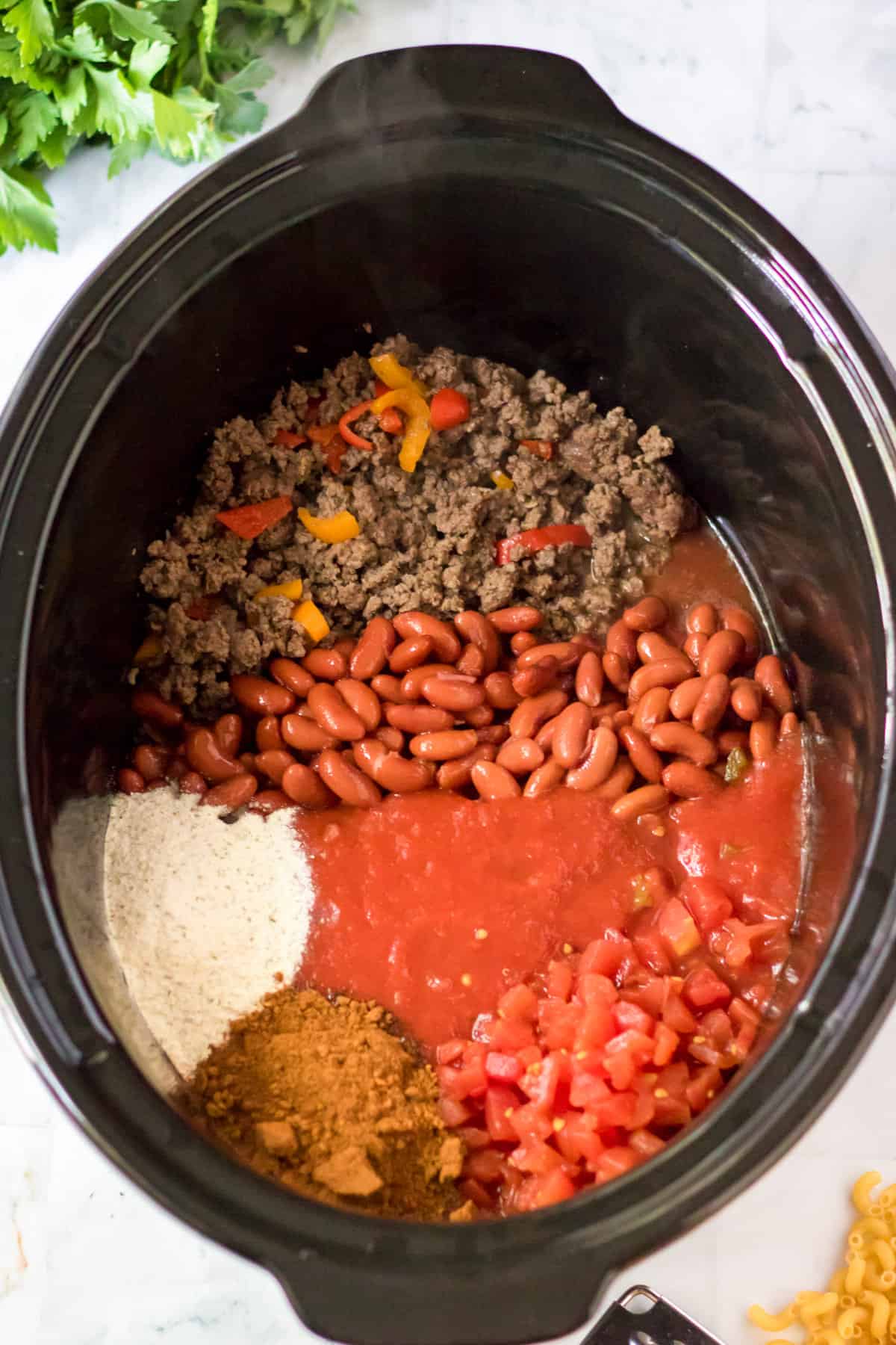 Ground beef, peppers, beans, rotel tomatoes, water, tomato sauce, and seasonings in slow cooker.