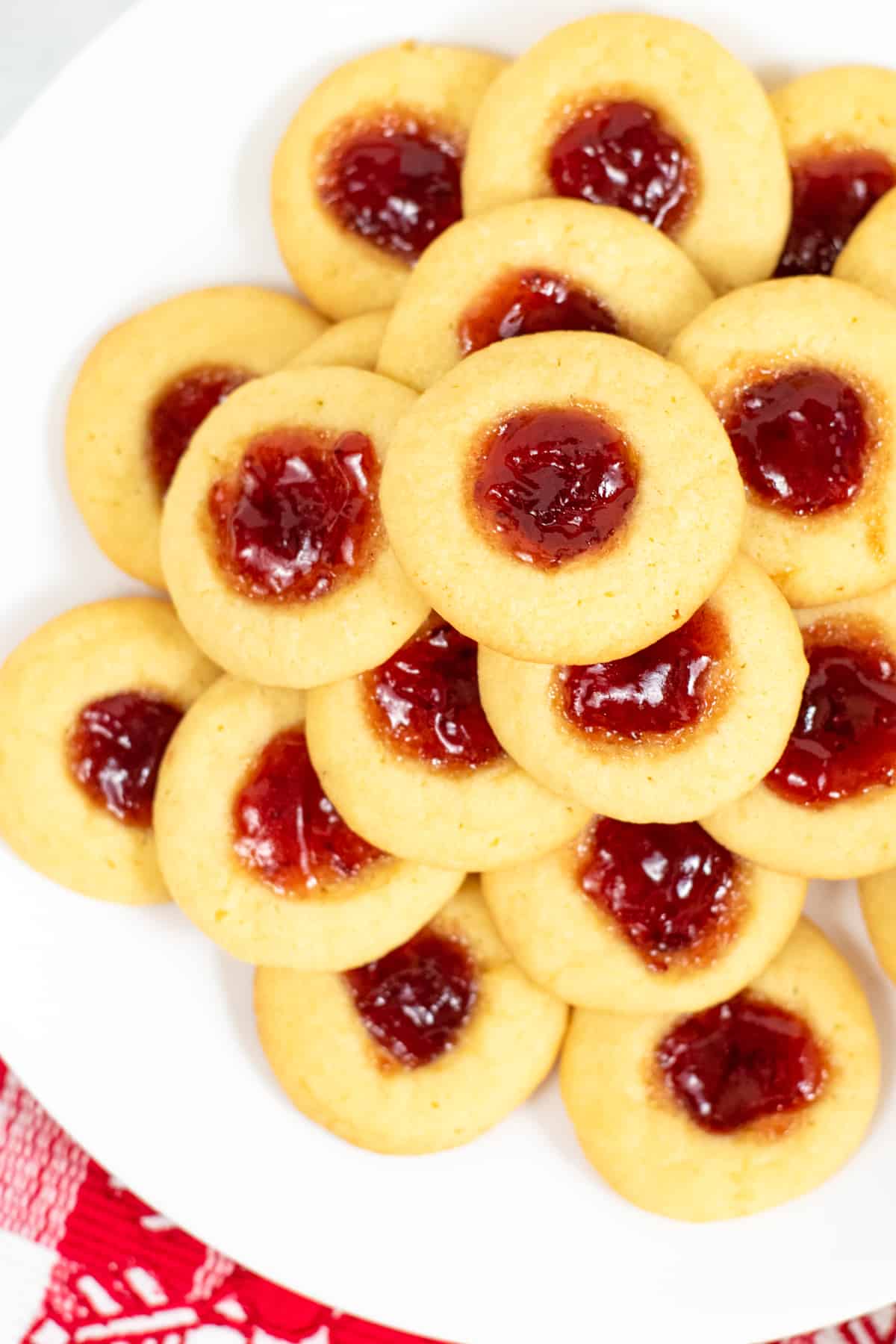 Top-down view of jam-filled thumbprint cookies stacked on white plate