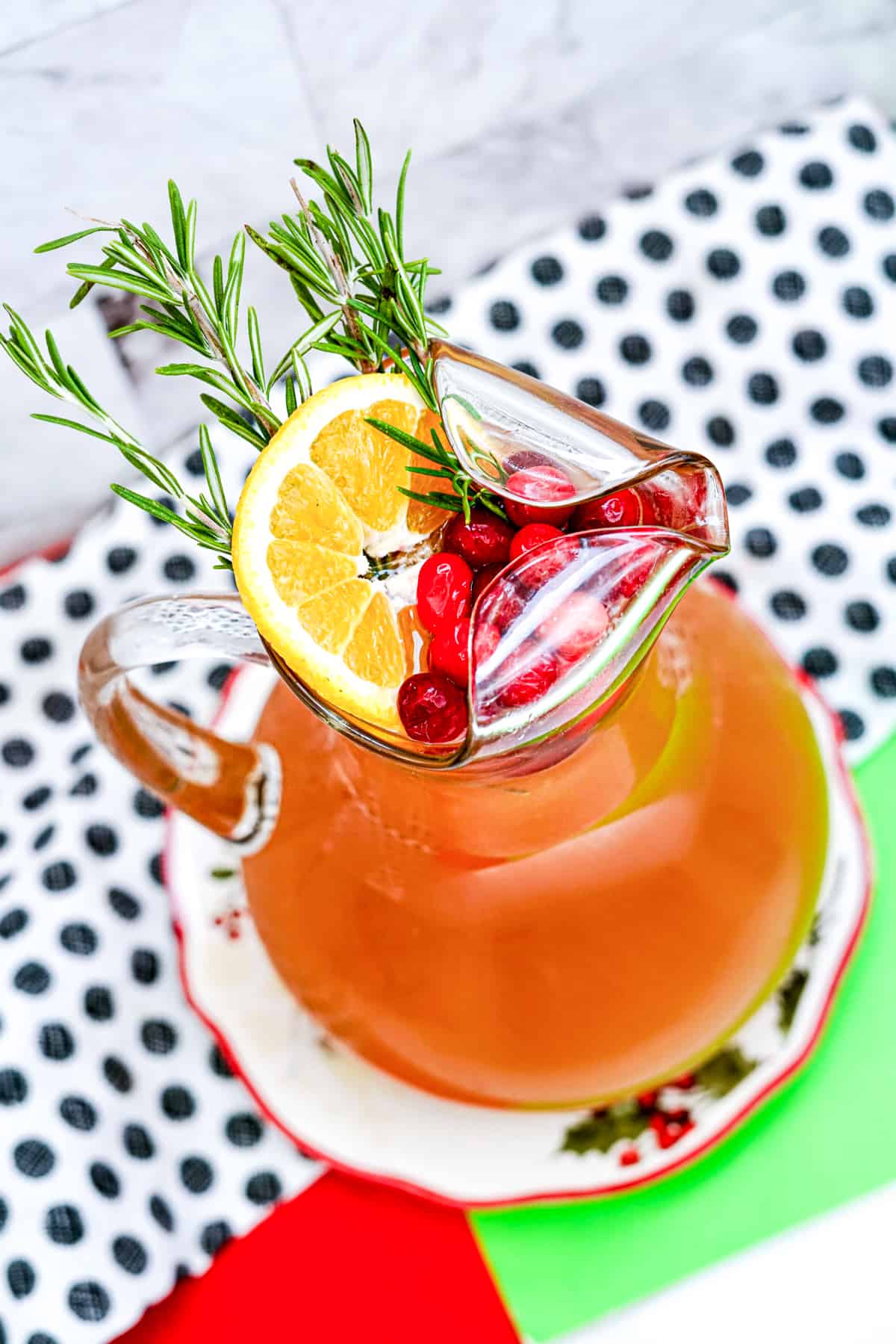 Overhead view of pitcher of punch garnished with rosemary, orange slice, and cranberries