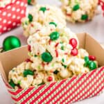 3 round Christmas Popcorn Balls with M&Ms and sprinkles in paper container for gifting with more popcorn balls in background