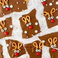 Chocolate reindeer bark broken into irregularly shaped pieces, each decorated with broken pretzels, candy eyes, and a red M&M to look like Rudolph the red-nosed reindeer