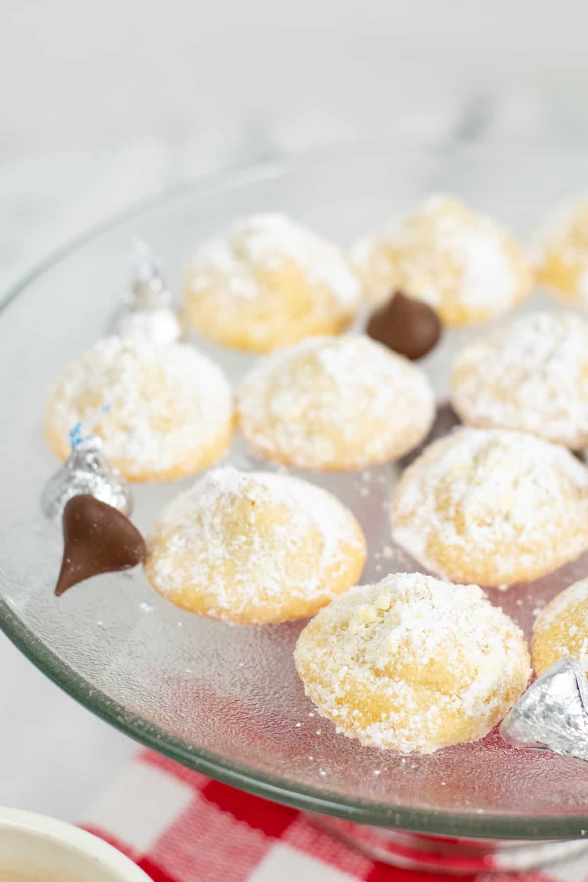 soft sugar cookies stuffed with chocolate kisses and rolled in powdered sugar. Unwrapped kisses are on platter with cookies.