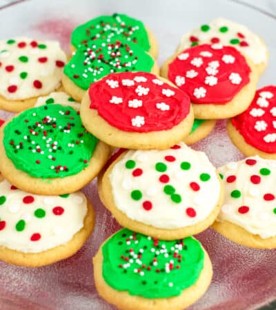 Platter of round frosted sugar cookies decorated with red, green, and white frosting and christmas sprinkles