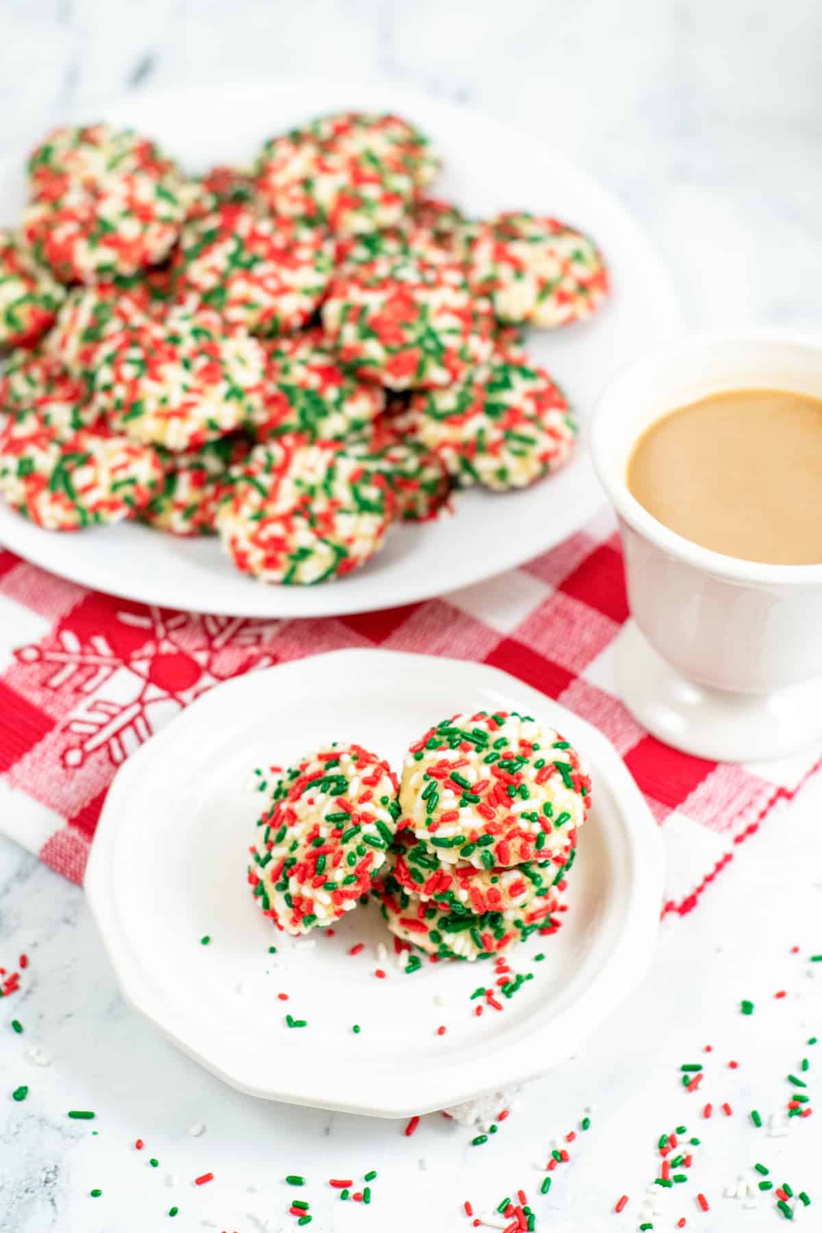 Soft christmas sprinkle cookies on large white plate and a smaller serving on small white plate with cup of coffee next to it