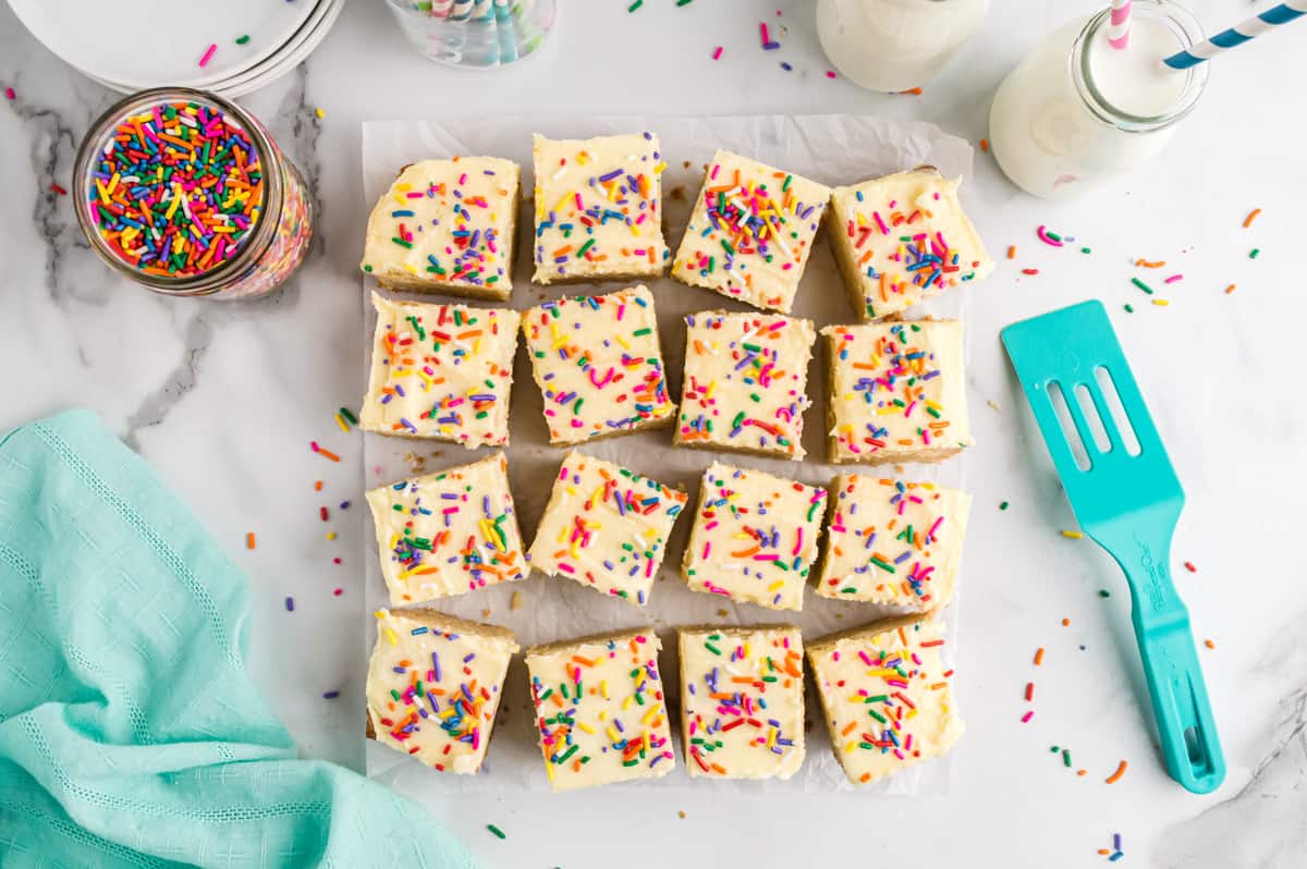 Sugar cookie bars baked in an 8 x 8 inch pan cut into squares, topped with icing and sprinkles