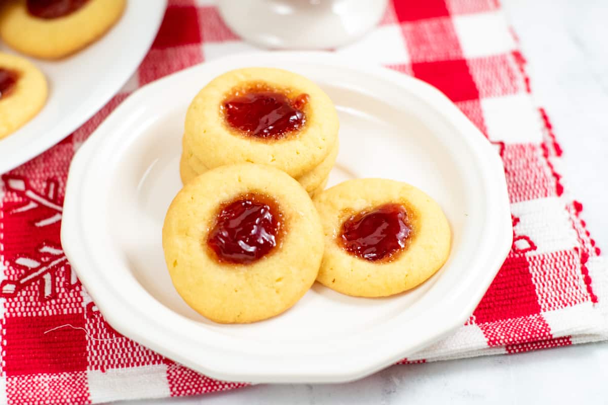Jam thumbprint cookies with strawberry jam on white plate with red and white checkered placemat under it