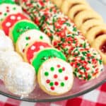 powdered sugar covered hidden kiss cookies, frosted Christmas cookies, sprinkle Christmas cookies, and thumbprint cookies with jam on a platter