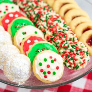 powdered sugar covered hidden kiss cookies, frosted Christmas cookies, sprinkle Christmas cookies, and thumbprint cookies with jam on a platter