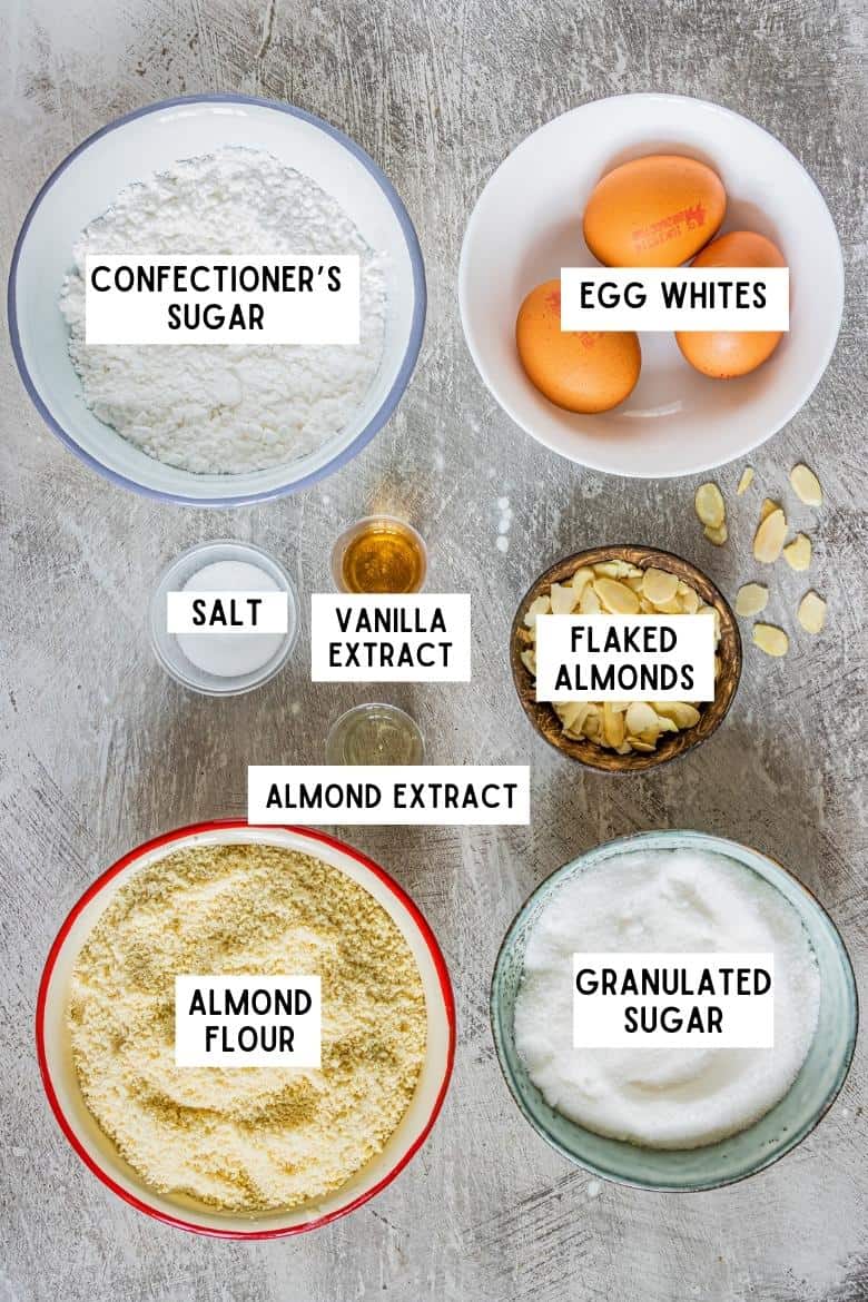 Ingredients on countertop: almond flour, granulated sugar, salt, confectioners sugar, 3 medium size eggs, vanilla extract, almond extract, flaked almonds 