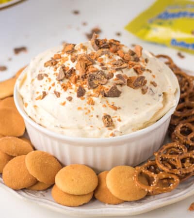 Butterfinger Candy Bar dessert dip with vanilla wafers and pretzels for dipping. Butterfinger candy bars and crunch bars in background.