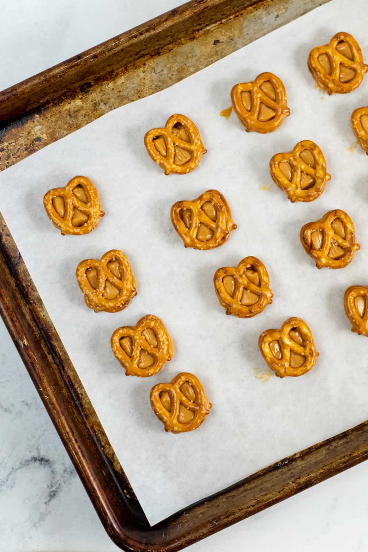 mini pretzels on baking sheet topped with melted caramel and another mini pretzel