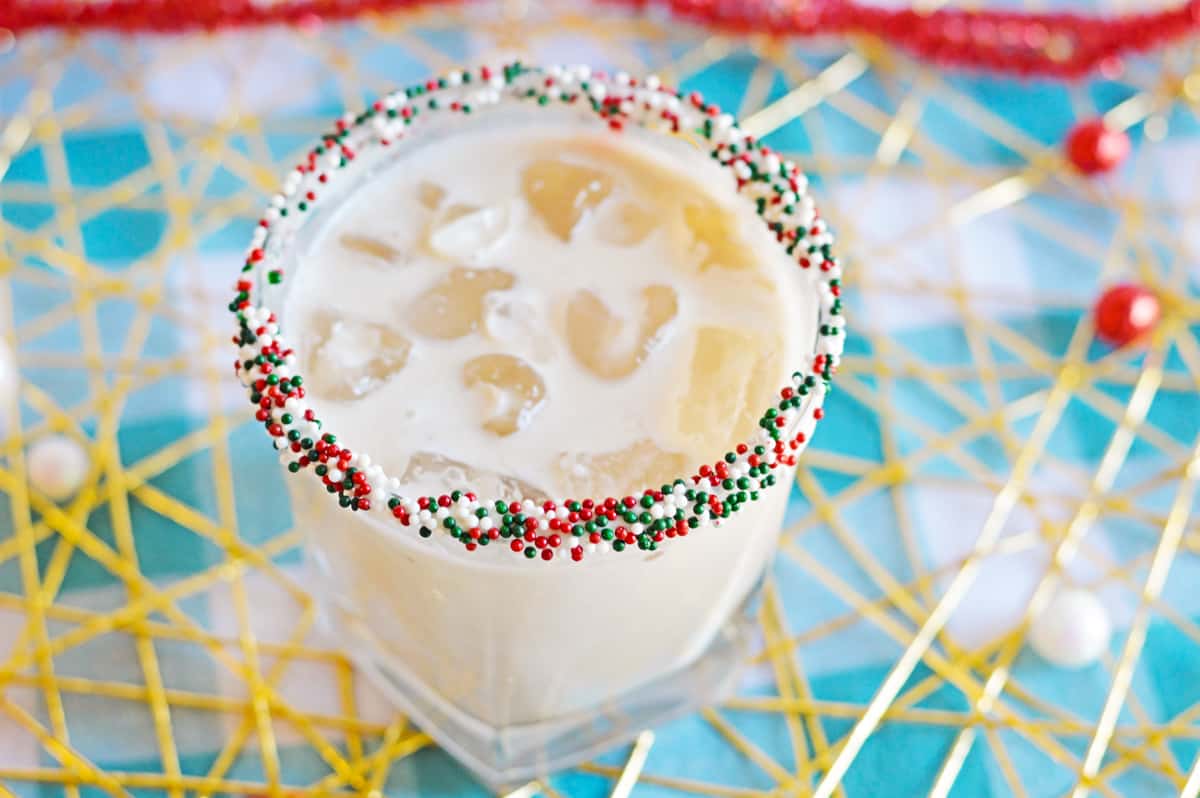 White creamy cocktail in glass with ice and cristmas sprinkles on rim