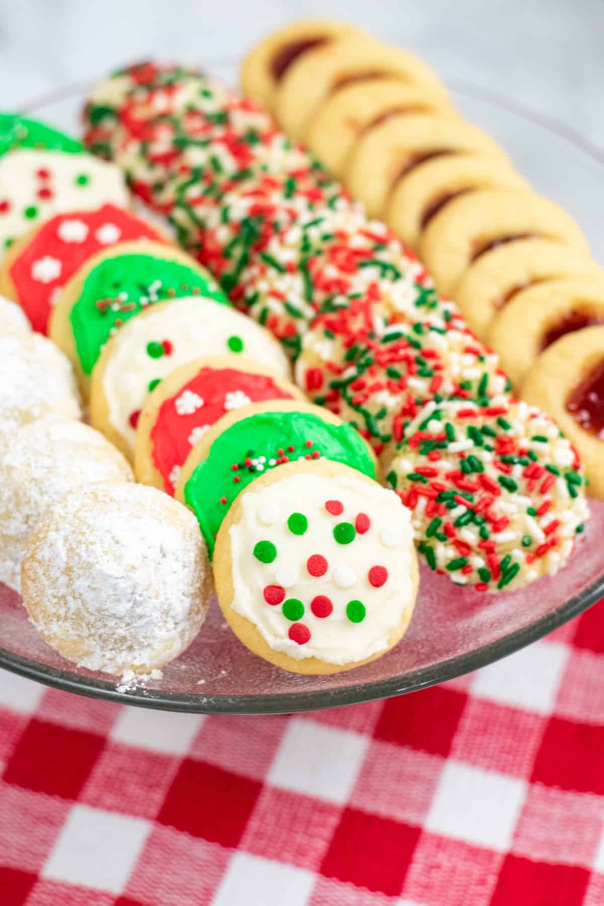 powdered sugar covered hidden kiss cookies, frosted Christmas cookies, sprinkle Christmas cookies, and thumbprint cookies with jam on a platter