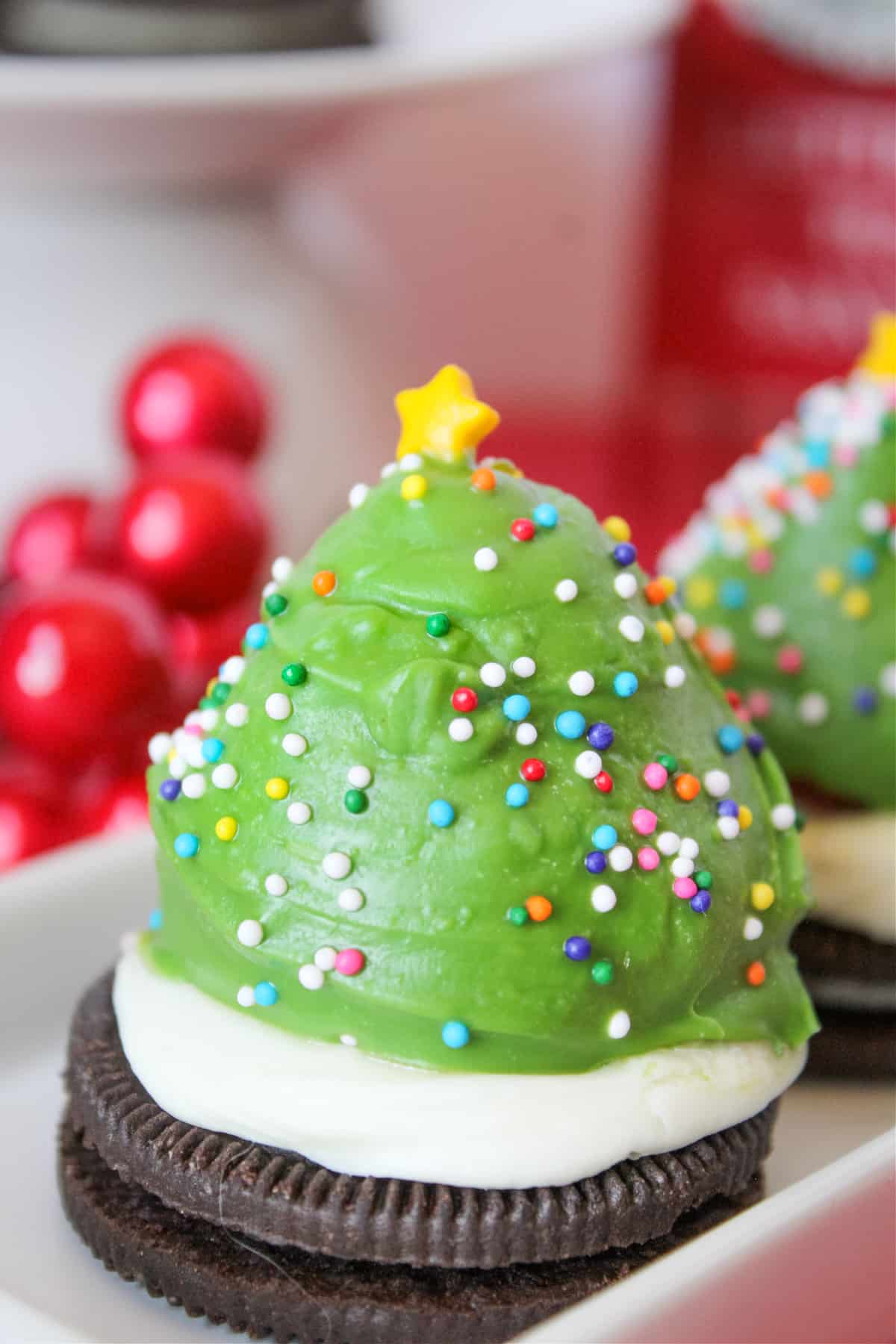 Strawberry dipped in green chocolate and decorated with sprinkles to look like a Christmas tree. The berry is sitting on an oreo cookie topped with vanilla frosting.