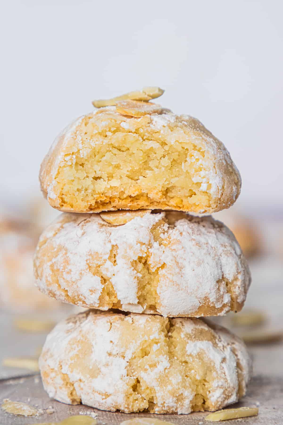 Three Italian Amaretti cookies on top of one another, with a top cookie broken in half to show soft, crumbly texture