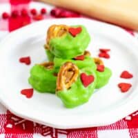 Grinch Pretzel Bites on white plate with red heart sprinkles sprinkled around them