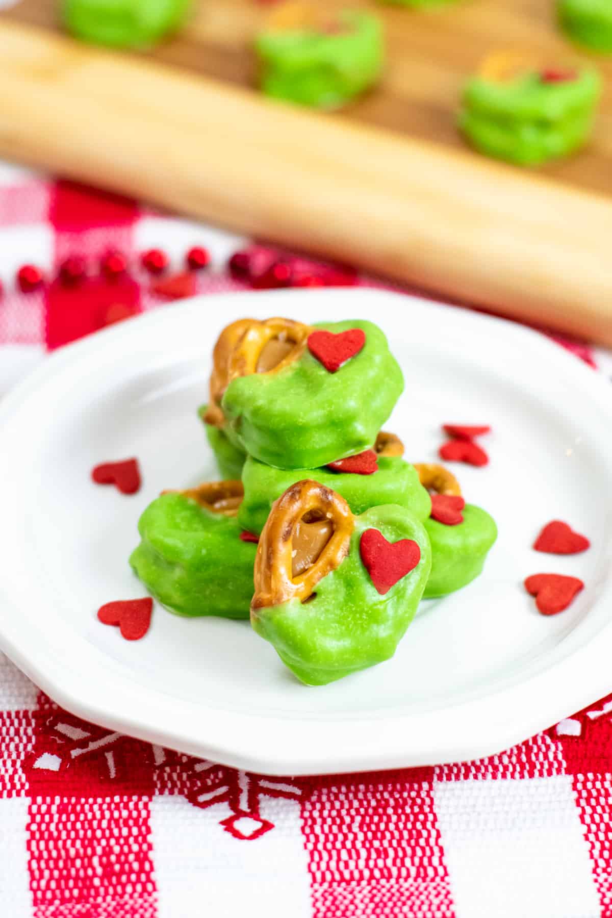 Grinch Pretzel Bites on white plate with red heart sprinkles sprinkled around them