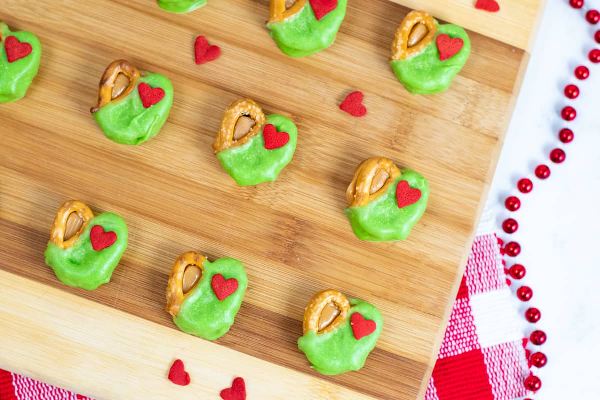 Grinch pretzel caramel bites dipped in green candy and topped with a red heart sprinkle. 