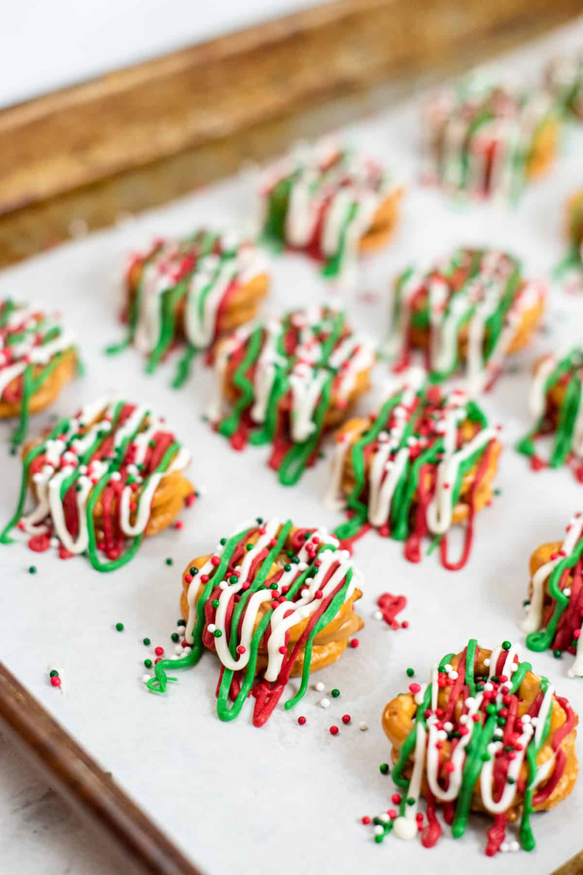 Pretzel Bites on parchment-lined baking sheet topped with red, green and white candy drizzles and christmas sprinkles