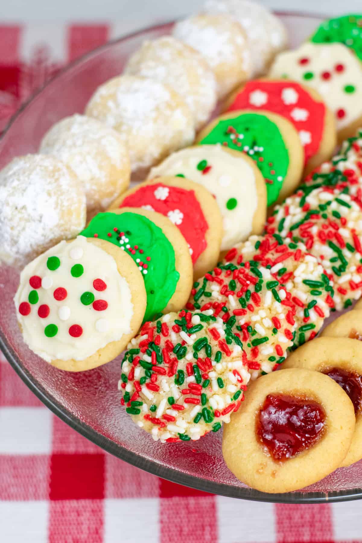 4 different Christmas Cookies on cookie tray: powdered sugar cookies, frosted cookies, sprinkle cookies, and jam cookies
