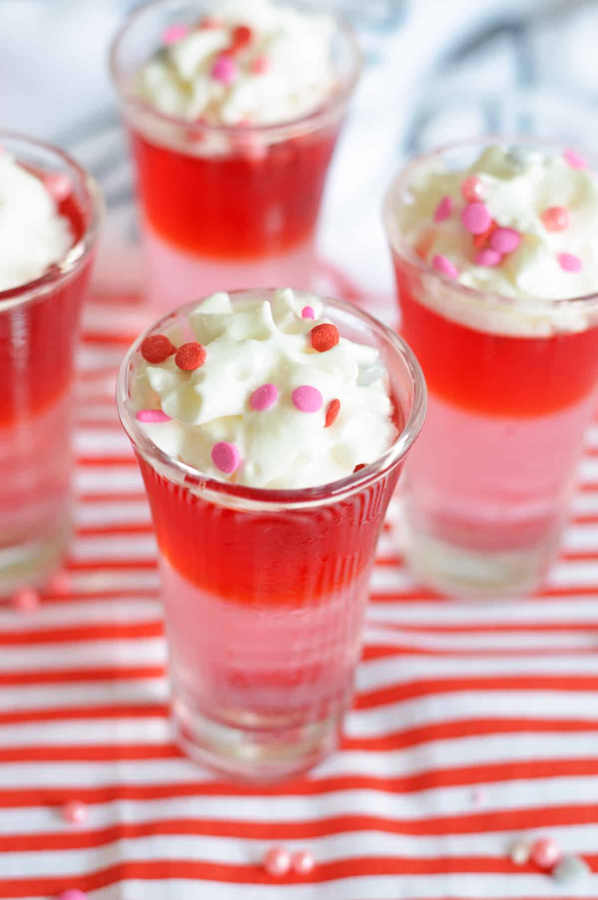 Red and pink layered Jello Shots toped with whipped cream and pink and red confetti sprinkles