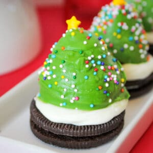 Strawberry dipped in green chocolate and decorated with sprinkles to look like a Christmas tree. The berry is sitting on an oreo cookie topped with vanilla frosting.