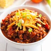 bowl of chili with beans and ground beef topped with shredded cheese and scallions