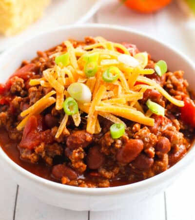 bowl of chili with beans and ground beef topped with shredded cheese and scallions