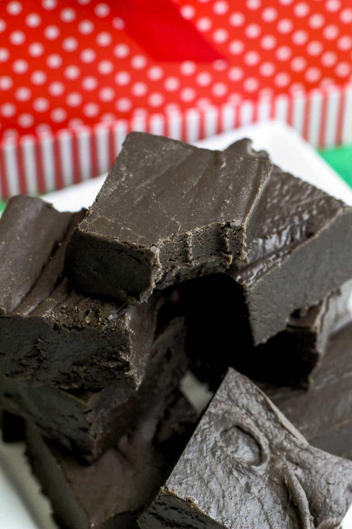 Pieces of black fudge stacked on white platter with christmas decor in background.