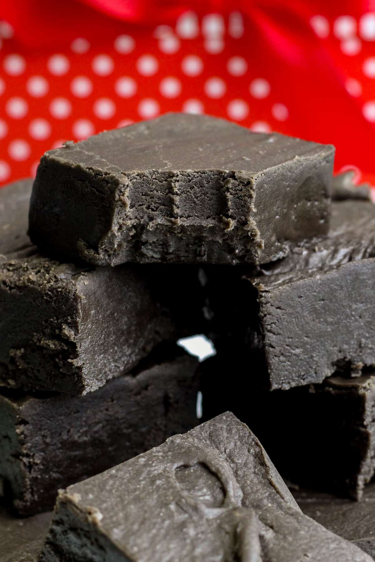Black fudge cut in squares and stacked in a pile. The top piece has a bite taken out of it.