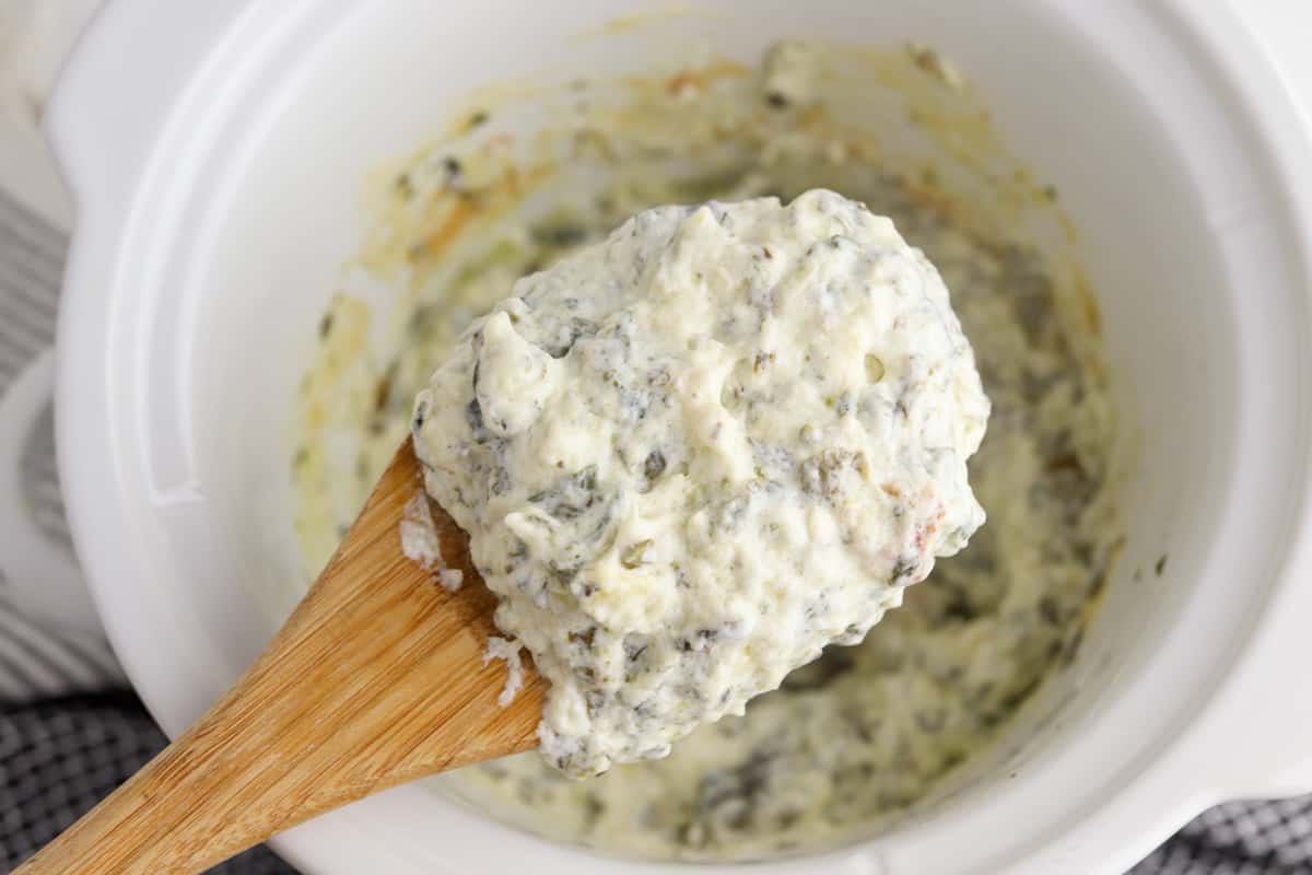 crockpot spinach artichoke dip with a wooden spoon scooping some of the dip out