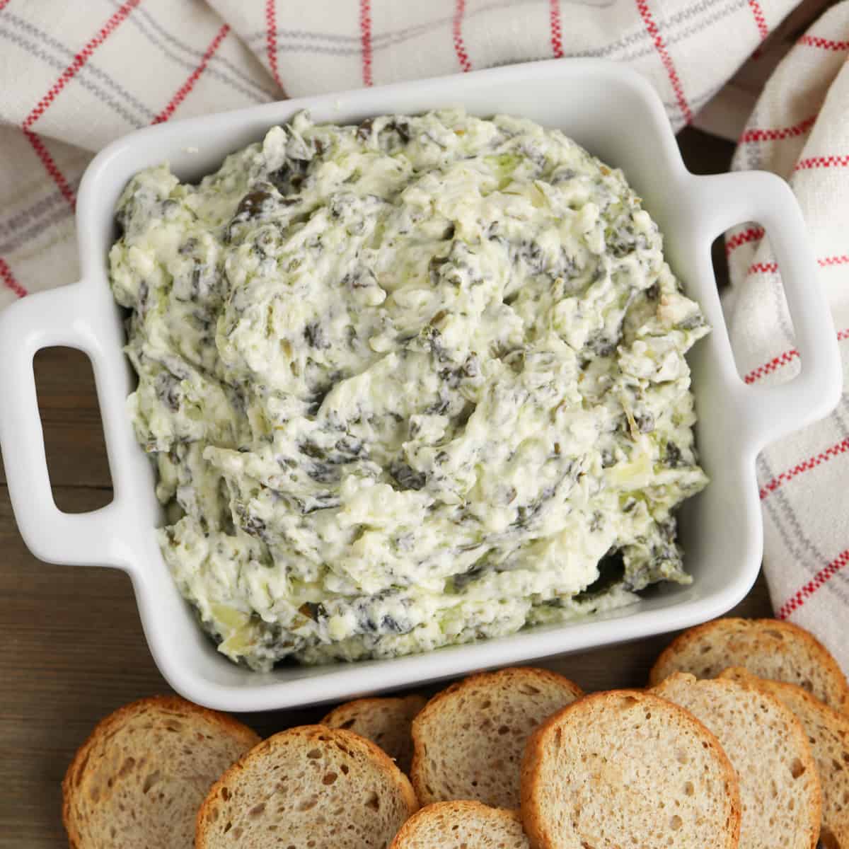 creamy crockpot spinach and artichoke dip in white bowl served with small pieces of bread for dipping
