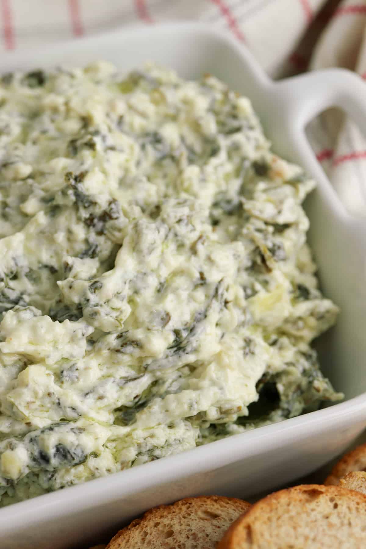 Creamy and cheesy slow cooker spinach artichoke dip in white serving bowl with small pieces of bread for dipping