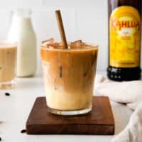 eggnog white russian cocktail with spoon in glass. Bottle of kahlua, eggnog, and another cocktail are in the background.