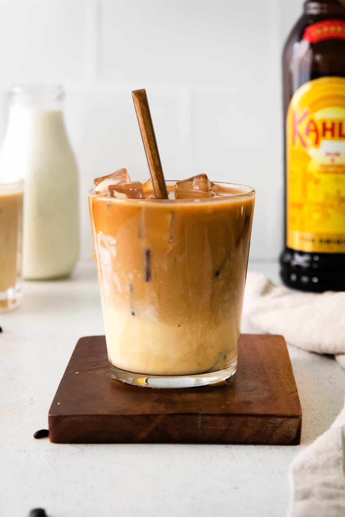 eggnog white russian cocktail with spoon in glass. Bottle of kahlua, eggnog, and another cocktail are in the background.