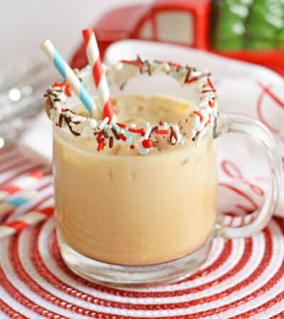 Gingerbread cocktail with vodka and kahlua in glass mug with sprinkles on rim and two paper straws. Christmas decor is in the background.