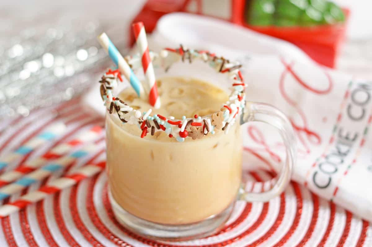 Gingerbread vodka cocktail in sprinkle-rimmed glass mug with paper straws and festive holiday decor in the background