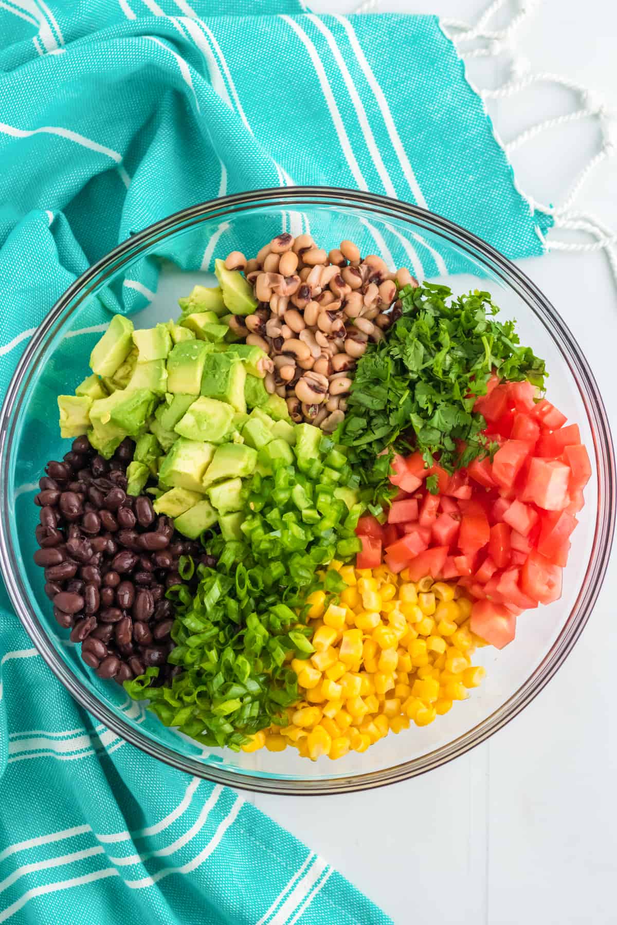 Corn, black beans, black eyed peas, and chopped avocado, jalapeño, scallions, tomatoes, and cilantro in a large mixing bowl.