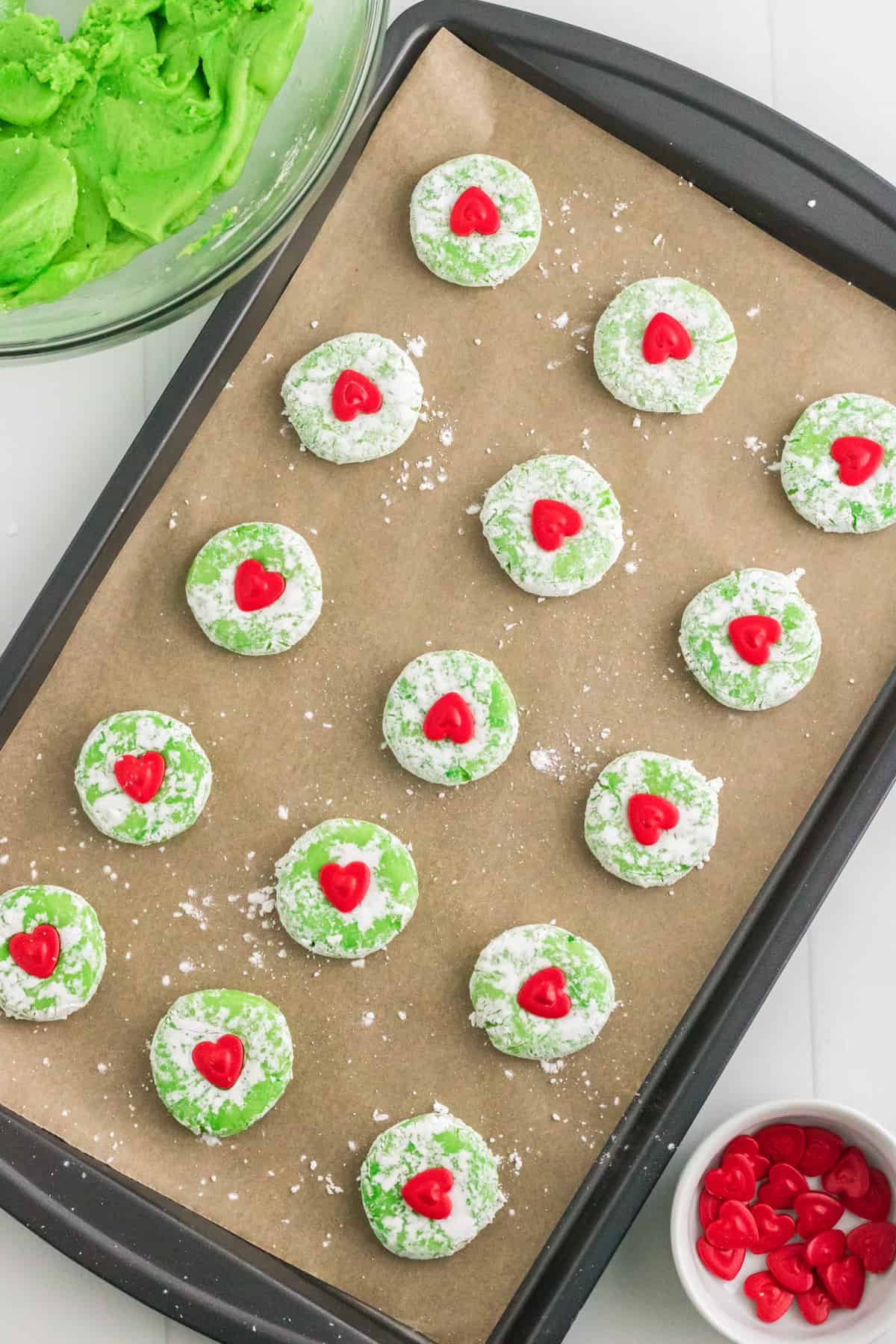 Parchment lined baking sheet with unbaked grinch cookies topped with red hearts