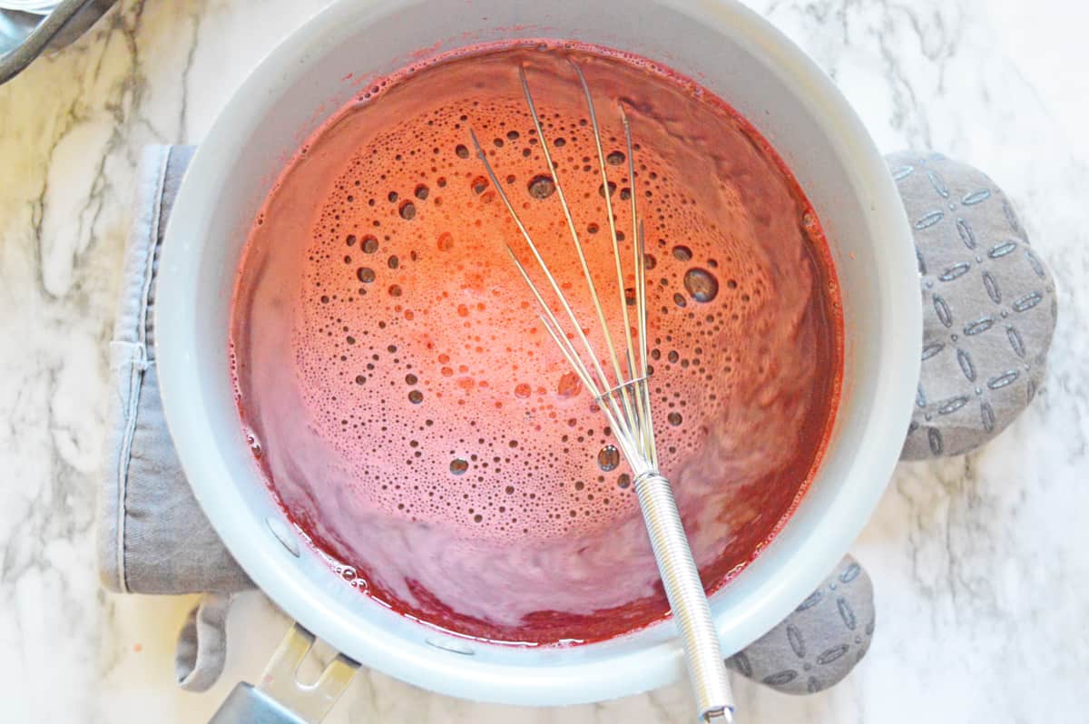 Bowl of strawberry jello shot mixture and wire whisk