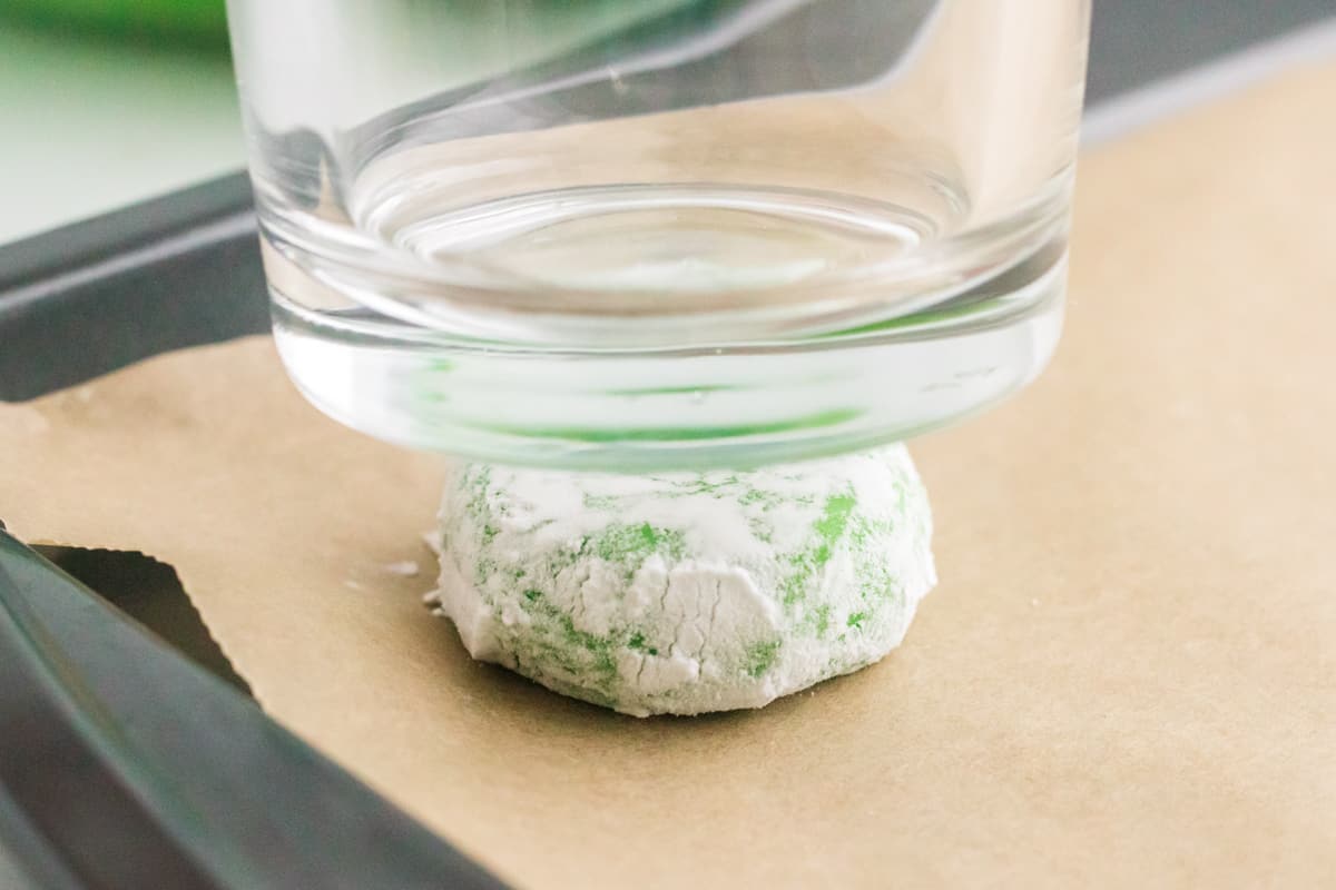 glass flattening green cookies on baking sheet