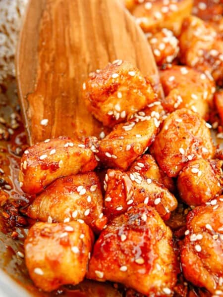 Wooden spoon stirring sesame chicken in skillet