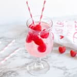 Pink Moscato Sangria with fresh raspberries in a cocktail glass with pink and white striped paper straws