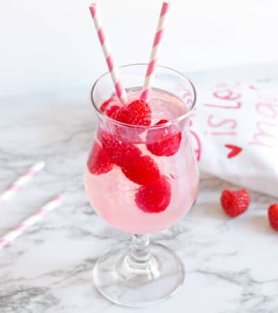 Pink Moscato Sangria with fresh raspberries in a cocktail glass with pink and white striped paper straws