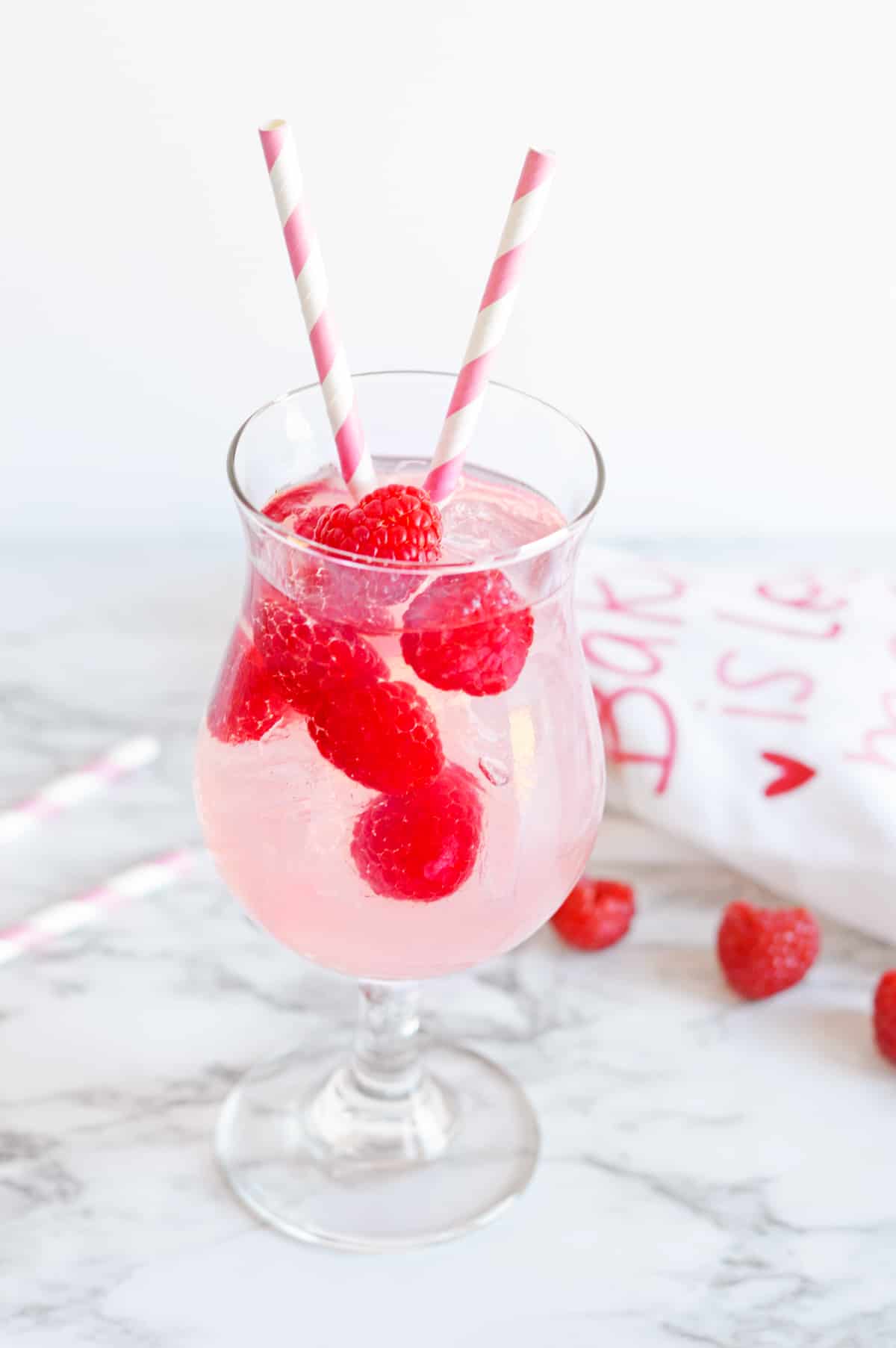 Pink Moscato Sangria with fresh raspberries in a cocktail glass with pink and white striped paper straws