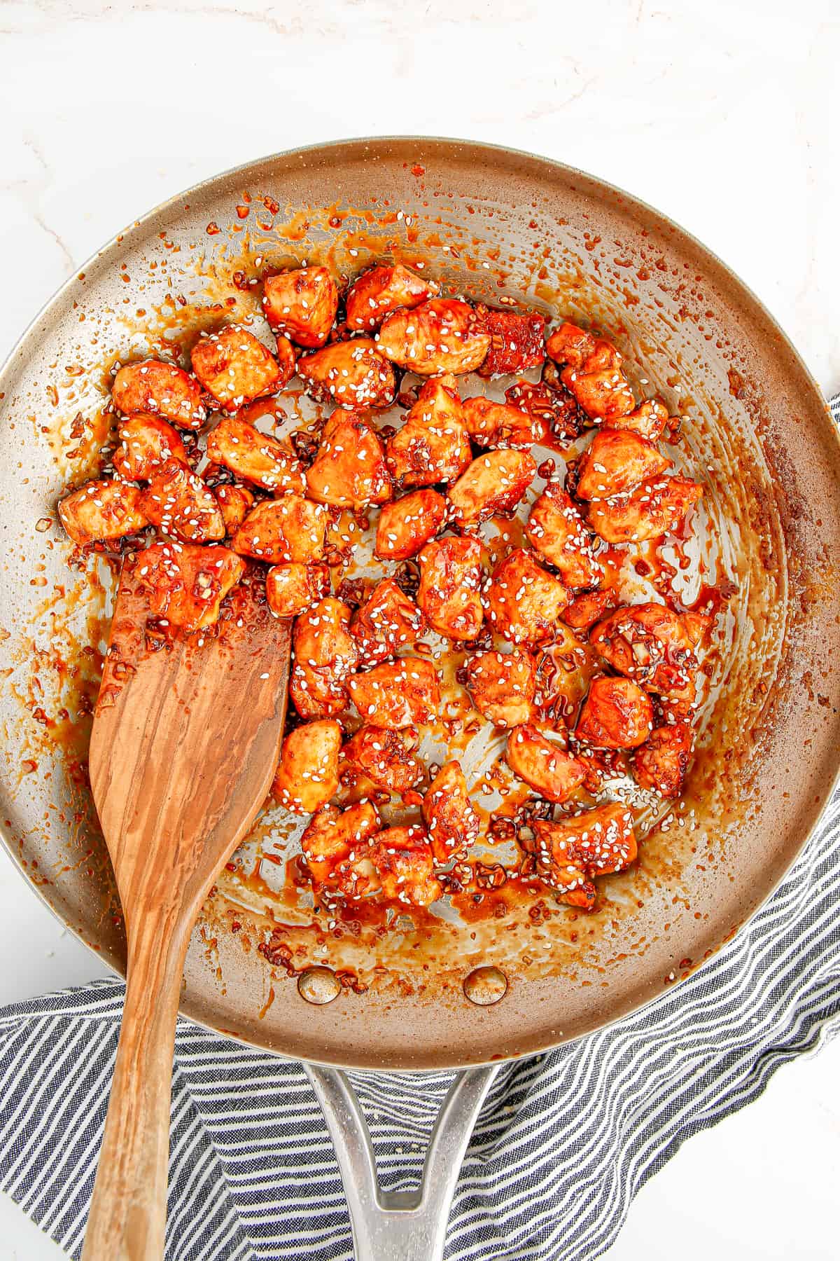 sesame chicken in skillet with wooden spoon