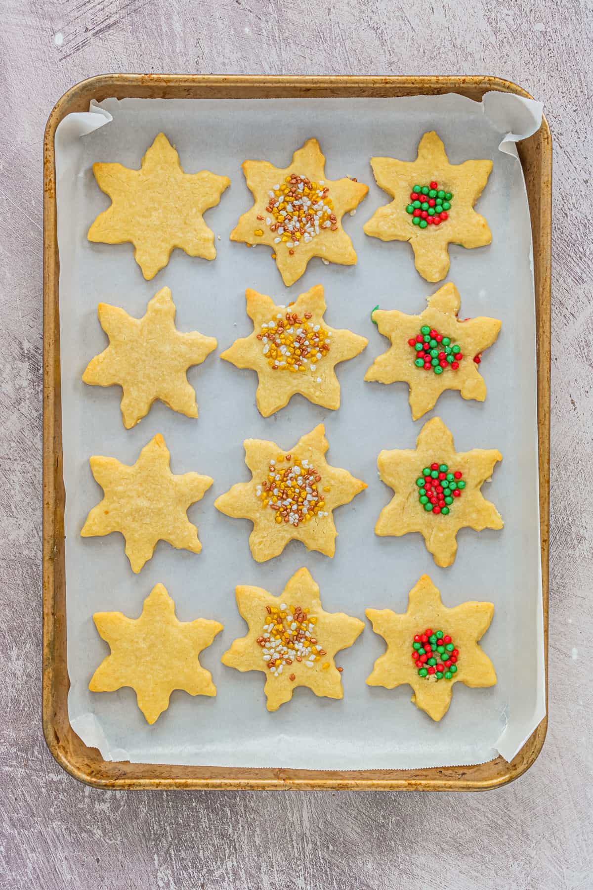 Snowflake Shortbread Cookies on lined baking sheet. Some are topped with sprinkles, others are plain